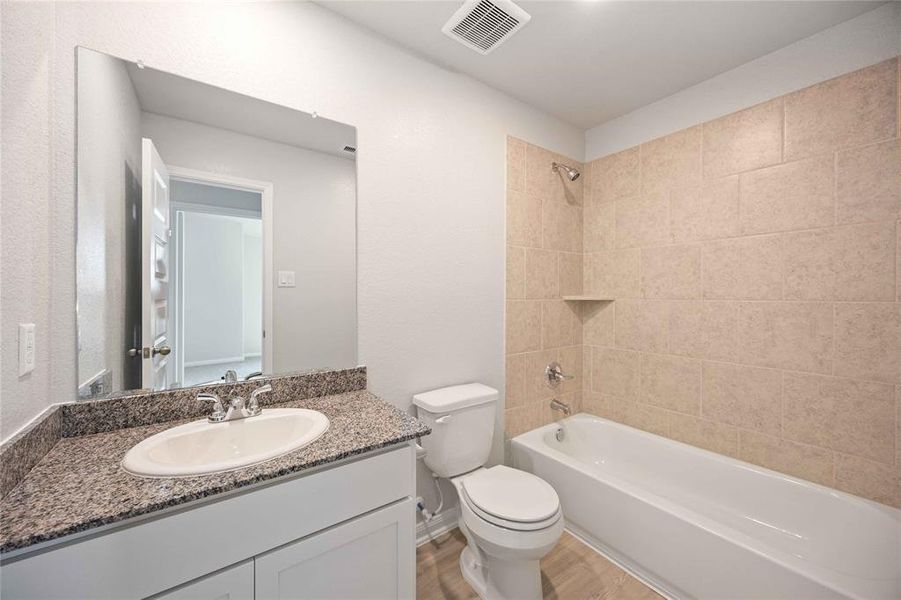 This secondary bathroom features a clean, modern design with a tiled shower and tub combo, a granite countertop, and a sleek under-mount sink. The bright white finishes create a fresh, airy feel, complemented by durable hardware and a five-panel door for added style.