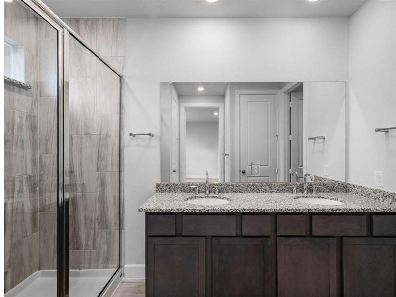 The primary bathroom includes a spacious shower and a double sink vanity with granite countertops, combining style and convenience for a luxurious experience.