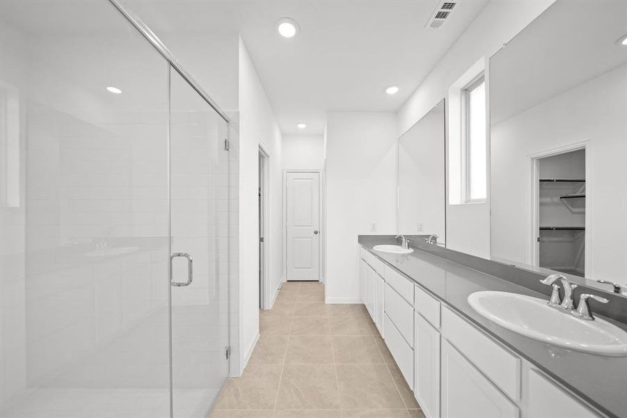 Spacious Primary bathroom featuring a quartz counter tops with double vanity with storage, a large mirror, a glass-enclosed tiled shower, and tile flooring. It is well-lit with recessed lighting and has a neutral color.