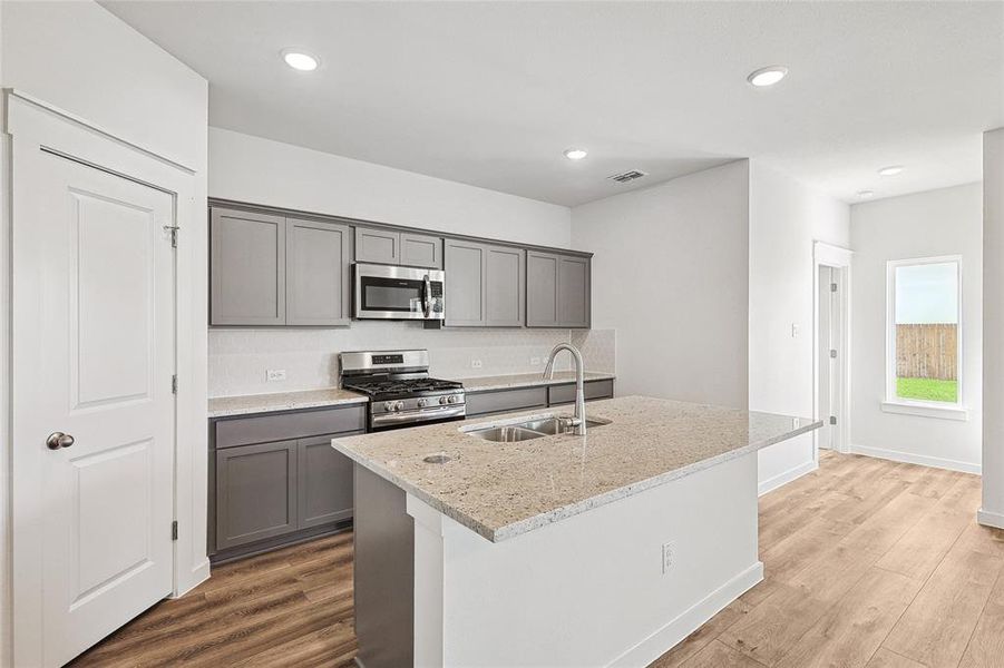 Kitchen featuring sink, light wood-type flooring, light stone countertops, gray cabinetry, and stainless steel appliances