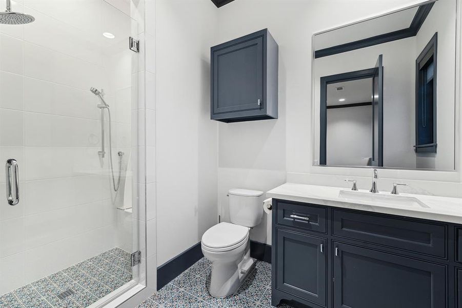 Each bedroom features an en suite bathroom. This particular bathroom features a walk-in shower adorned with stunning tile flooring, complemented by a white countertop and sleek dark cabinetry.
