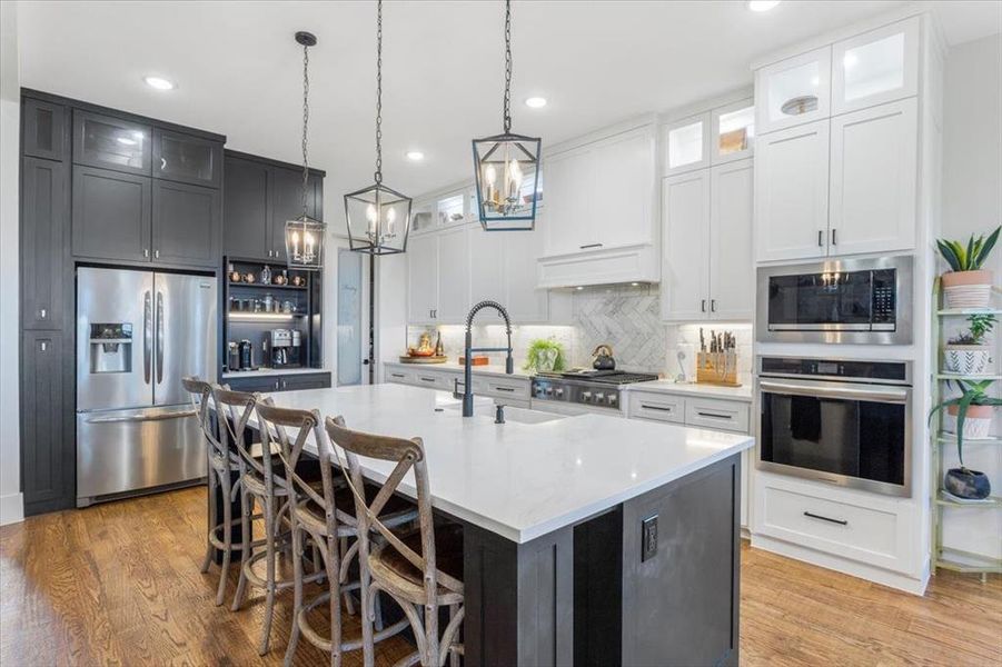 Kitchen with light hardwood / wood-style floors, a kitchen island with sink, sink, custom exhaust hood, and appliances with stainless steel finishes