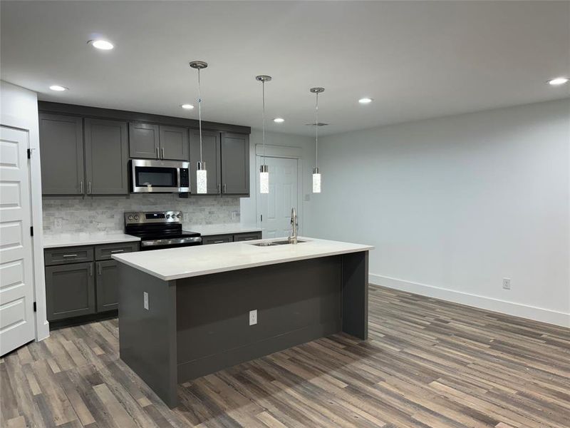 Kitchen featuring dark wood-type flooring, pendant lighting, stainless steel appliances, and sink