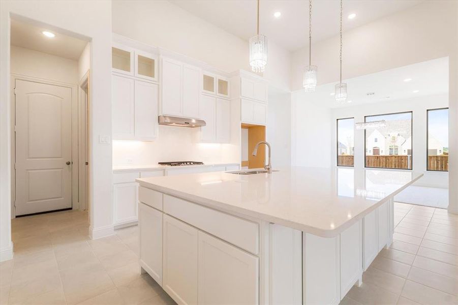 Kitchen featuring white cabinetry, a center island with sink, decorative light fixtures