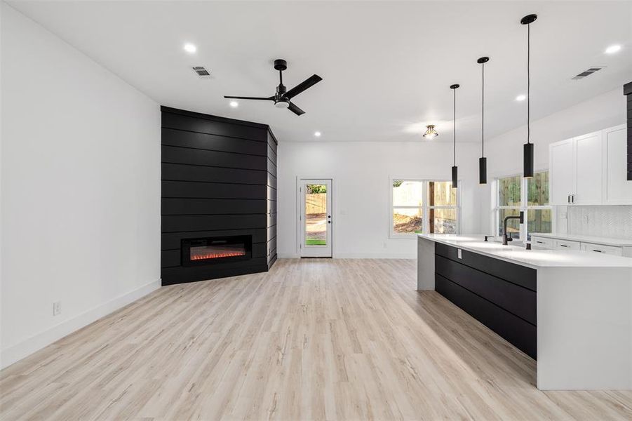 Kitchen featuring a fireplace, light wood-type flooring, an island with sink, ceiling fan, and pendant lighting