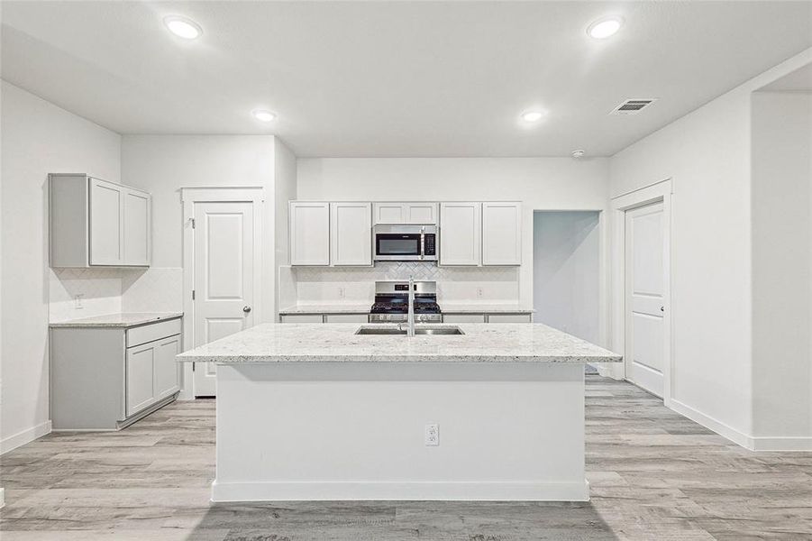 Kitchen with decorative backsplash, stainless steel appliances, sink, and an island with sink