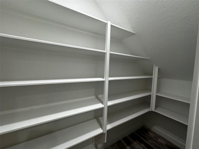 This is a spacious, well-organized walk-in closet with multiple white shelves, providing ample storage options for clothing and accessories.