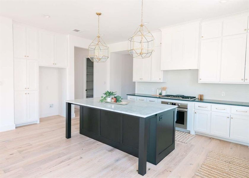 Kitchen featuring hanging light fixtures, white cabinets, a kitchen island, light wood-type flooring, and oven