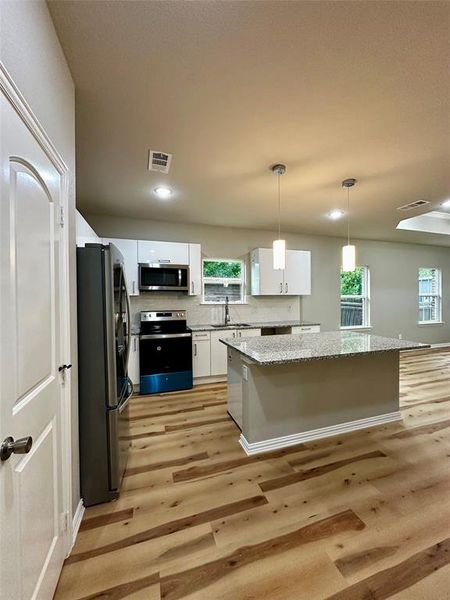 Kitchen with white cabinetry, hanging light fixtures, sink, light hardwood / wood-style floors, and appliances with stainless steel finishes