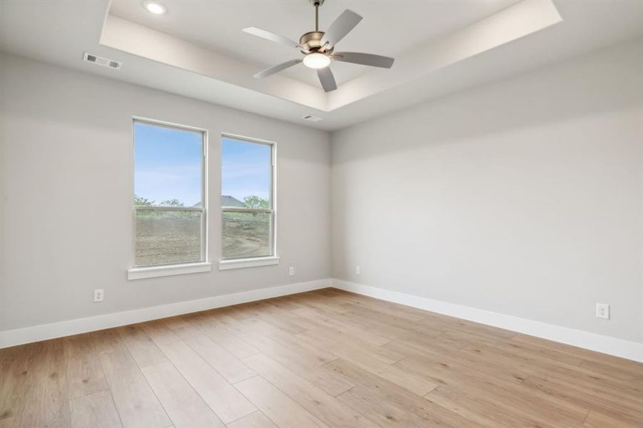 Empty room with light hardwood / wood-style floors, a tray ceiling, and ceiling fan