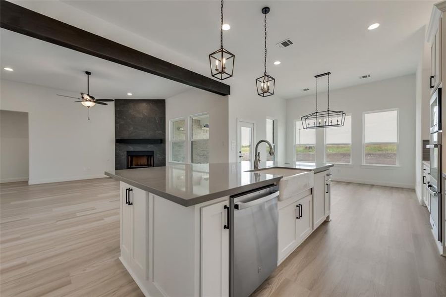 Kitchen with stainless steel dishwasher, a center island with sink, light wood-type flooring, ceiling fan with notable chandelier, and white cabinets