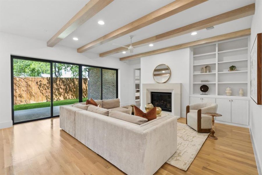 Living room featuring light wood-type flooring, beam ceiling, ceiling fan, and built in features