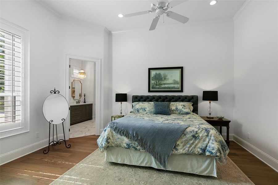This spacious secondary bedroom is downstairs and could easily be another primary bedroom. Complete with wood floors, crown molding, double base boards, shutters, and a ceiling fan!