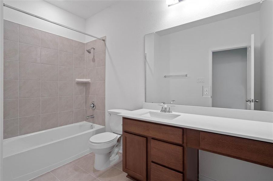 Secondary bath features tile flooring, bath/shower combo with tile surround, stained wood cabinets, beautiful light countertops, mirror, sleek fixtures and modern finishes.