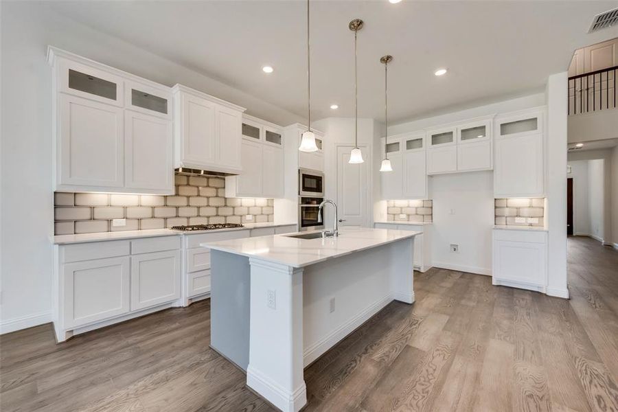Kitchen featuring a center island with sink, tasteful backsplash, hardwood / wood-style floors, and stainless steel appliances