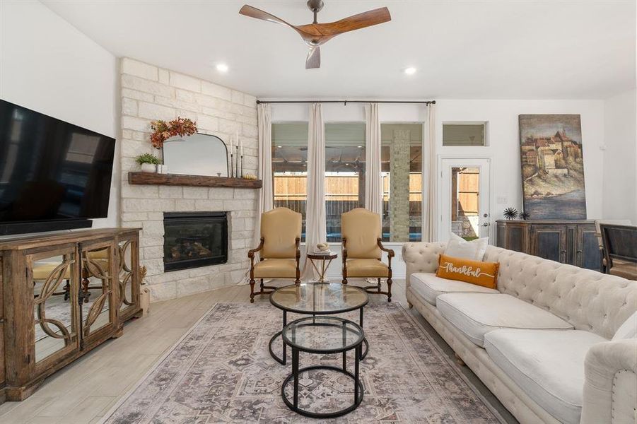 Living room featuring ceiling fan, a stone fireplace, and light wood-type flooring