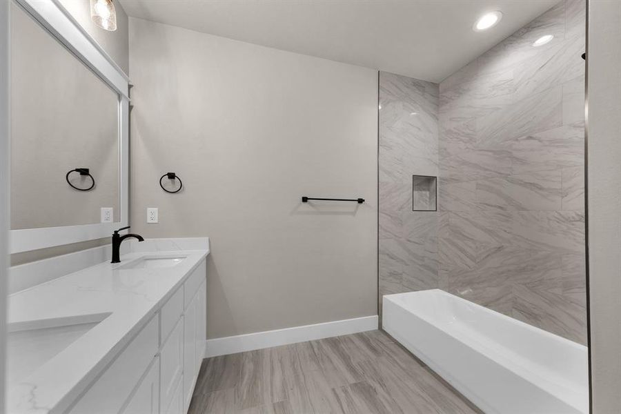 Bathroom with dual sinks, vanity with extensive cabinet space, and tiled shower / bath