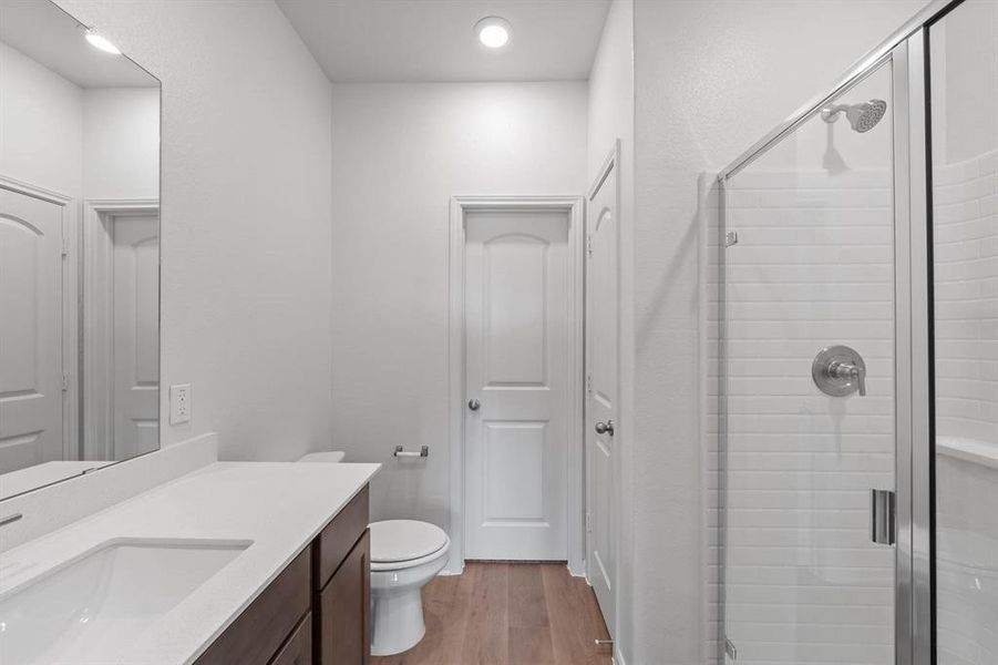 Bathroom featuring wood-type flooring, vanity, toilet, and a shower with door