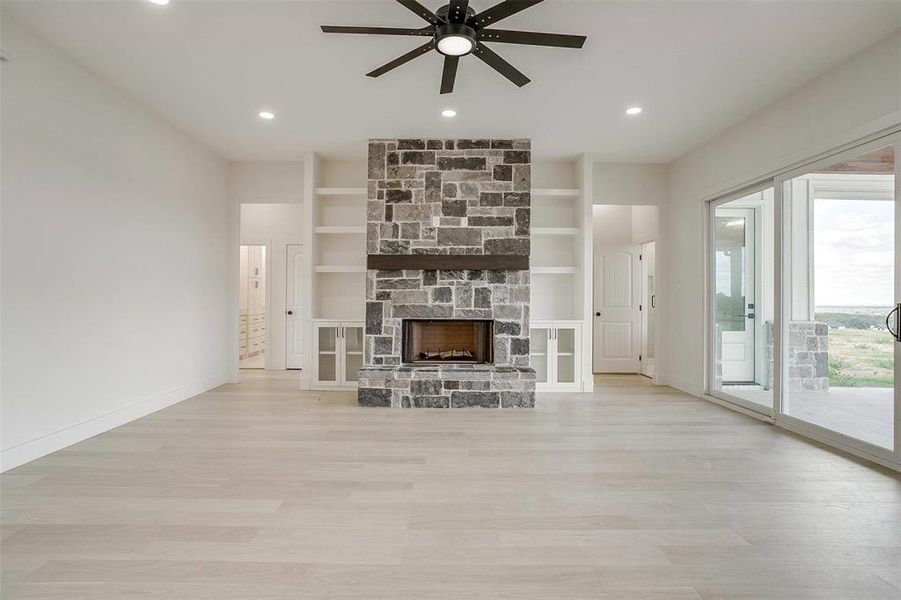 Unfurnished living room with light hardwood / wood-style floors, built in shelves, ceiling fan, and a stone fireplace