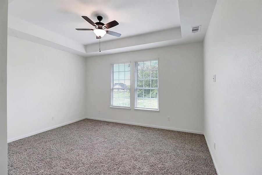 Carpeted empty room with ceiling fan and a raised ceiling