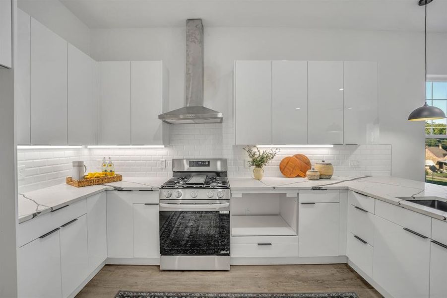 Kitchen with hanging light fixtures, wall chimney range hood, stainless steel gas range, and white cabinets