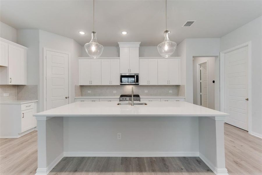 Kitchen with tasteful backsplash, white cabinets, stainless steel appliances, light hardwood / wood-style floors, and a large island with sink