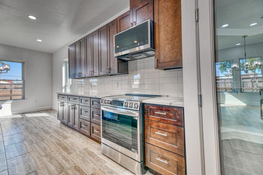 Kitchen featuring dark brown cabinetry, appliances with stainless steel finishes, a notable chandelier, and backsplash