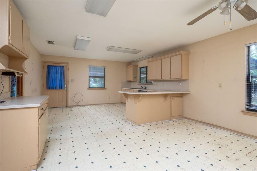 Kitchen with light brown cabinetry, a breakfast bar area, kitchen peninsula, and ceiling fan