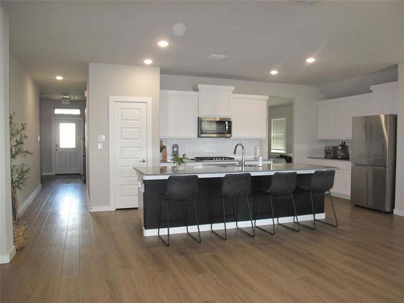 Kitchen with an island with sink, dark hardwood / wood-style floors, white cabinets, a breakfast bar area, and appliances with stainless steel finishes