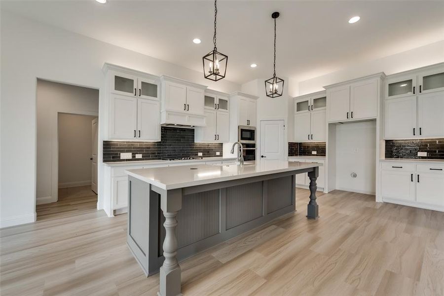 Kitchen featuring an island with sink, light hardwood / wood-style flooring, backsplash, and appliances with stainless steel finishes