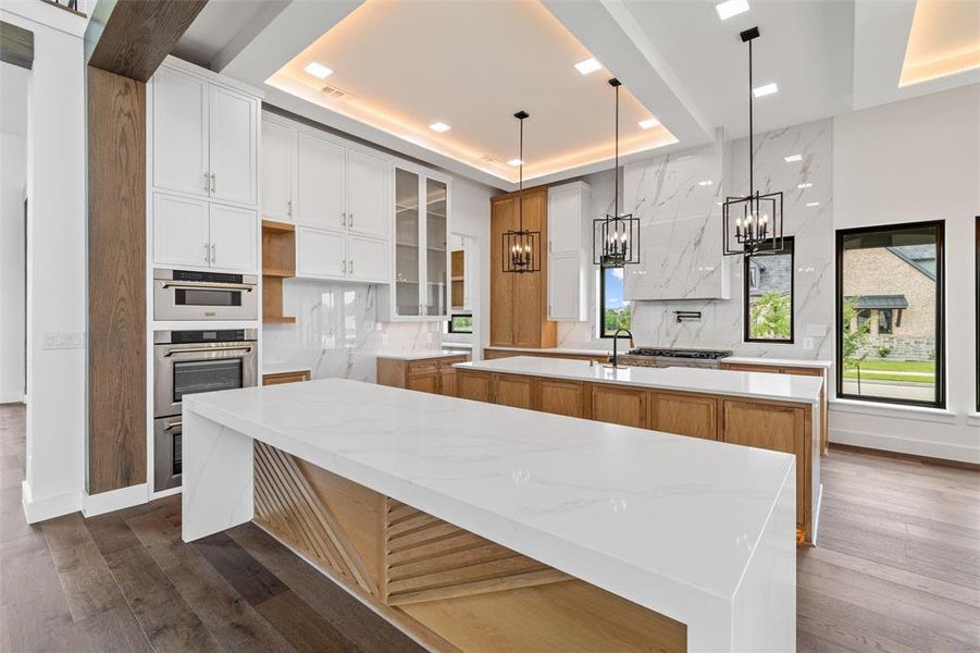 Kitchen featuring light stone countertops, hanging light fixtures, an island with sink, a tray ceiling, and dark hardwood / wood-style floors