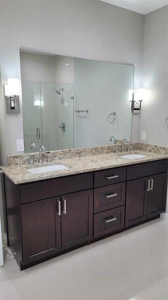 Bathroom with dual vanity, tile patterned floors, and a shower with door