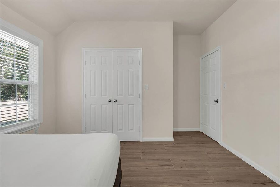 This is a well-lit, neutral-toned bedroom featuring tile flooring, a large window with blinds.