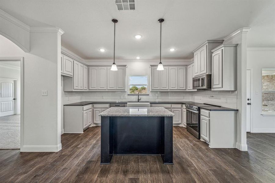 Kitchen with tasteful backsplash, hanging light fixtures, a kitchen island, appliances with stainless steel finishes, and dark wood-type flooring