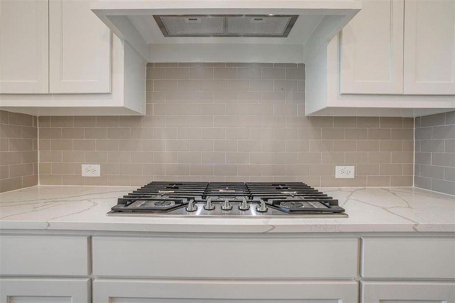 Kitchen with tasteful backsplash, white cabinets, and stainless steel gas stovetop