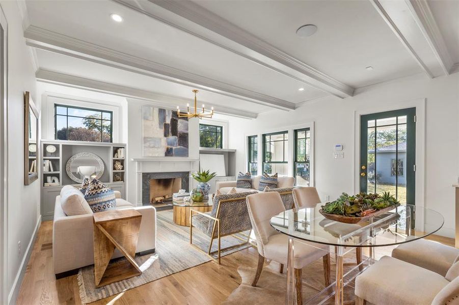 Dining space featuring beamed ceiling, light hardwood / wood-style flooring, a fireplace, and a chandelier