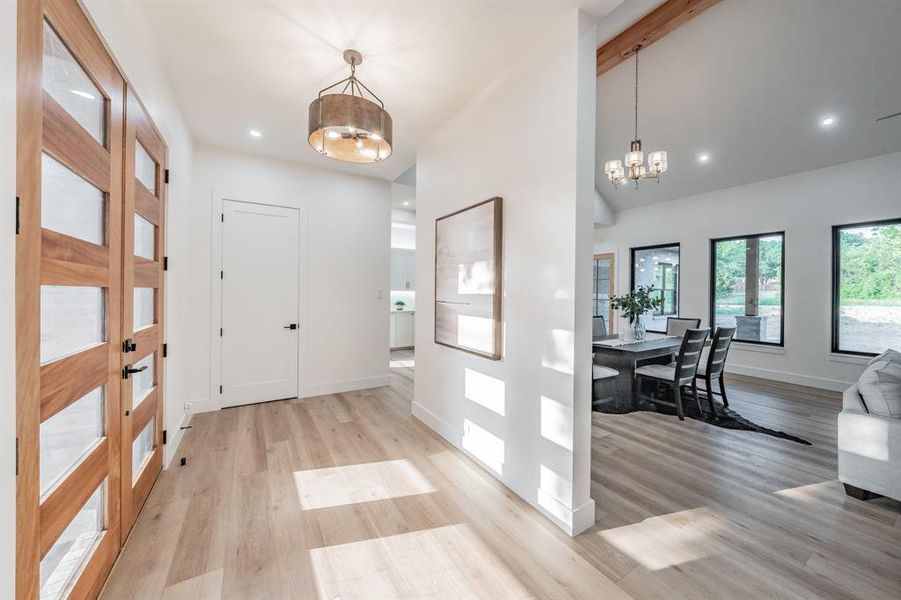 Entrance foyer featuring beam ceiling, blonde plank, wood-like luxury vinyl floors. and an inviting chandelier