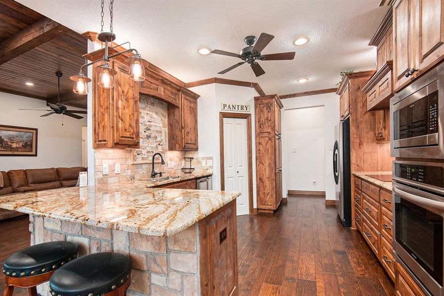 Kitchen with kitchen peninsula, stainless steel appliances, a breakfast bar, decorative light fixtures, and dark hardwood / wood-style flooring