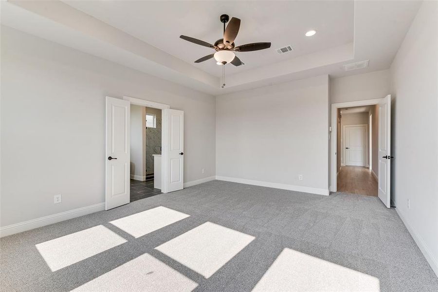 Unfurnished bedroom with a tray ceiling, dark carpet, and ceiling fan