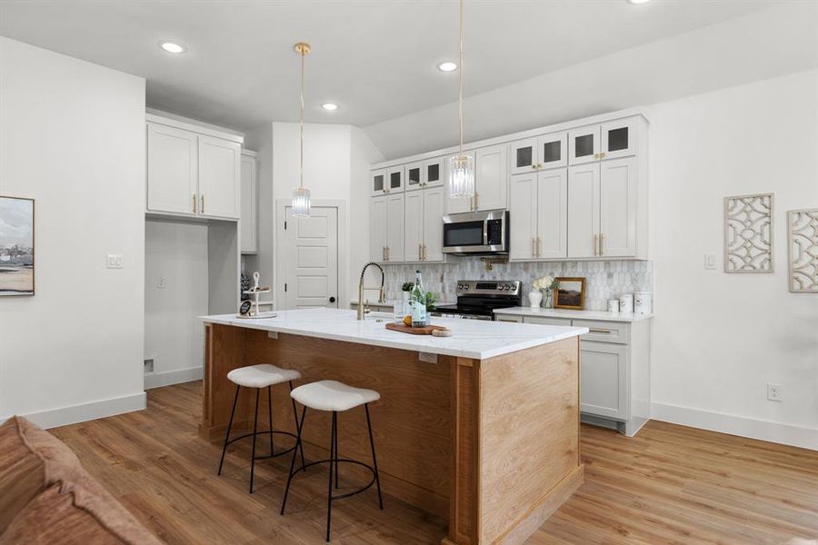 Kitchen featuring decorative light fixtures, a center island with sink, white cabinetry, stainless steel appliances, and light wood-type flooring