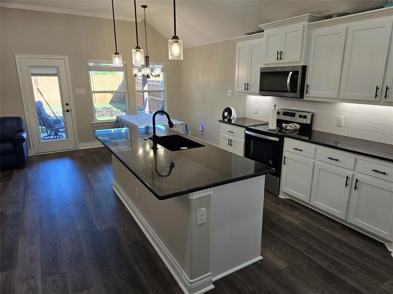 Kitchen with appliances with stainless steel finishes, white cabinetry, dark hardwood / wood-style floors, a center island with sink, and sink