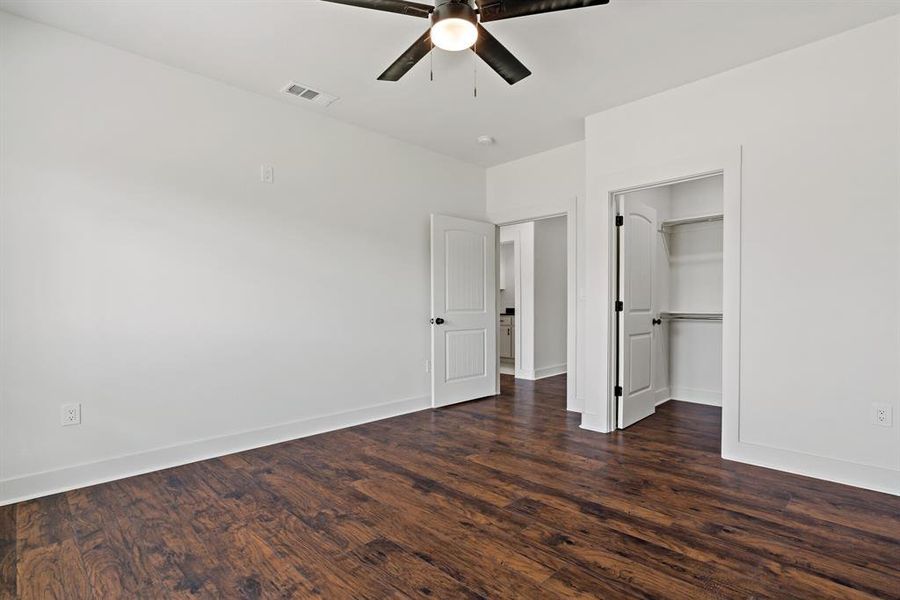 Unfurnished bedroom with a spacious closet, dark hardwood / wood-style floors, ceiling fan, and a closet