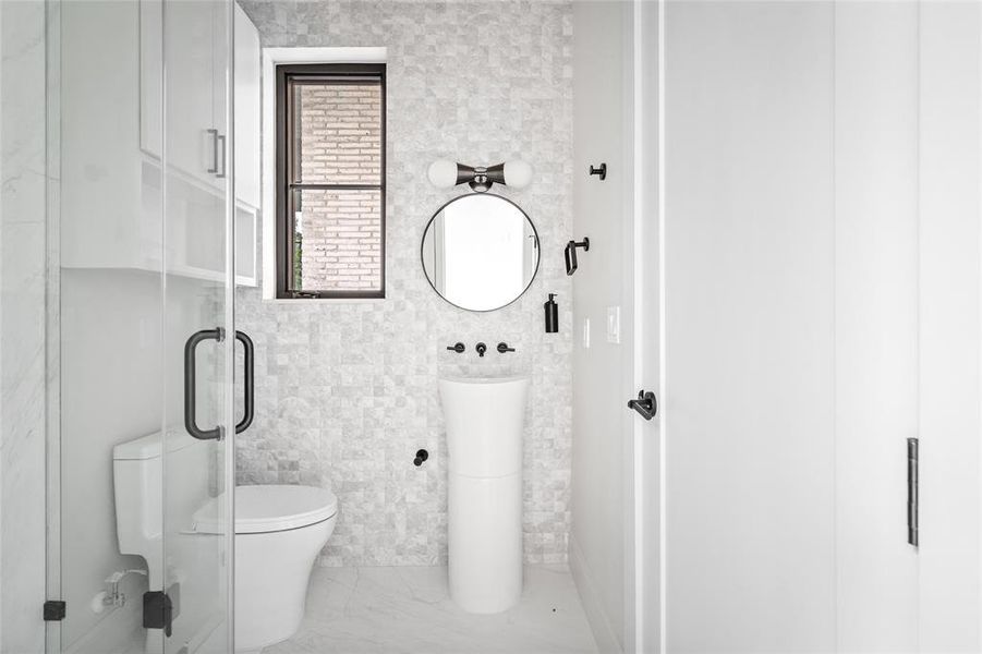 The ensuite bathroom exudes a simple yet sleek and chic aesthetic, boasting elegant tile walls, bespoke finishes, and a sophisticated walk-in shower, which is conveniently accessible to the pool area, allowing guests to freshen up and change after a refreshing swim.