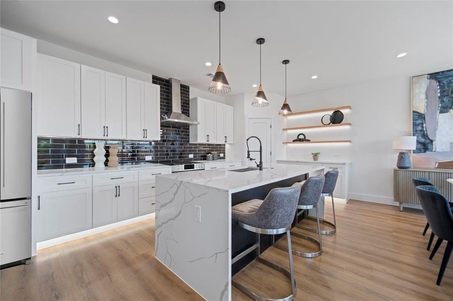 Kitchen with white fridge, white cabinets, light wood-type flooring, and wall chimney exhaust hood