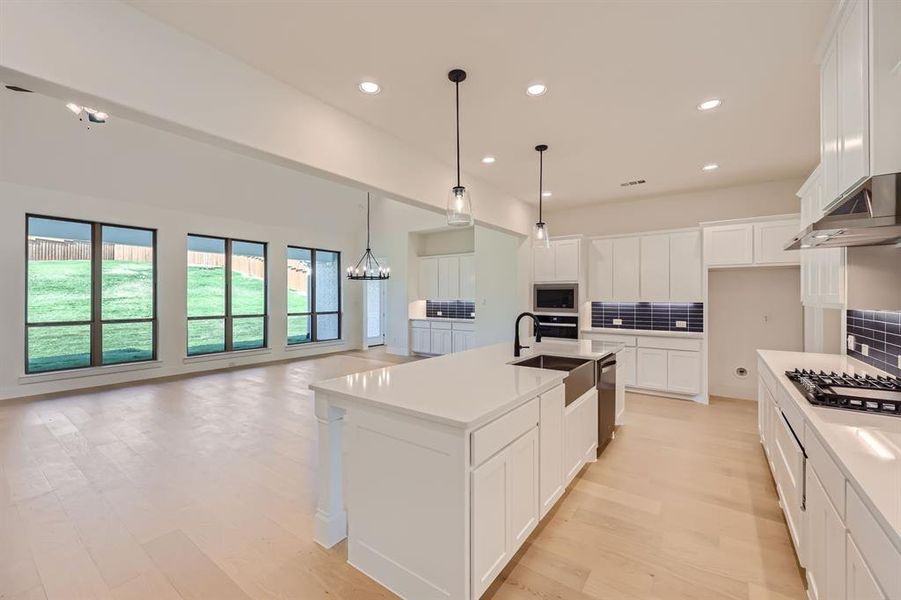 Kitchen with appliances with stainless steel finishes, white cabinets, a kitchen island with sink, and tasteful backsplash