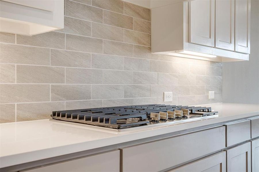 Kitchen with stainless steel gas cooktop, tasteful backsplash, and white cabinetry