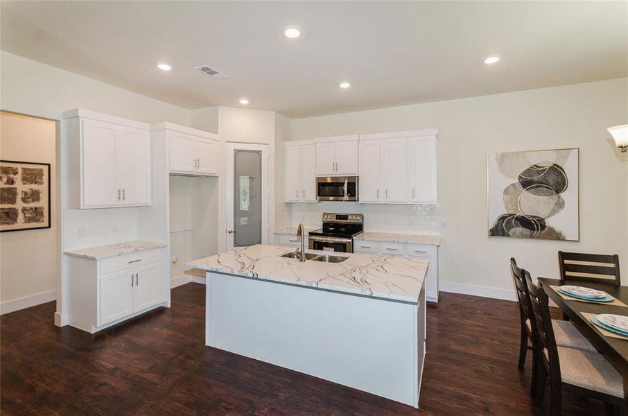 Kitchen featuring dark hardwood / wood-style floors, backsplash, a kitchen island with sink, white cabinets, and appliances with stainless steel finishes