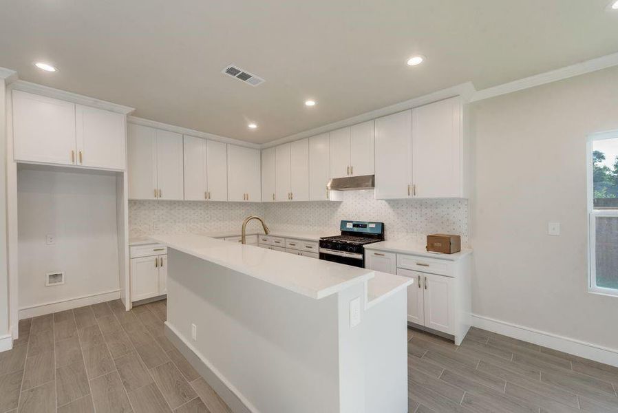 Kitchen with backsplash, stainless steel gas range oven, and white cabinets