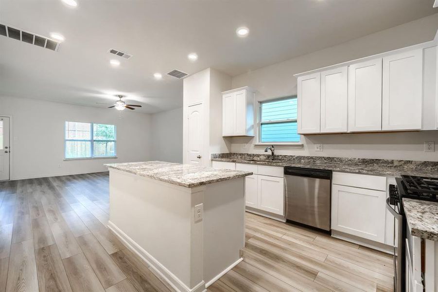 Kitchen featuring a center island, light wood-type flooring, white cabinetry, appliances with stainless steel finishes, and light stone counters