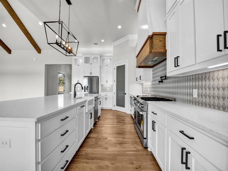 Kitchen with appliances with stainless steel finishes, custom exhaust hood, white cabinets, hardwood / wood-style flooring, and a kitchen island with sink